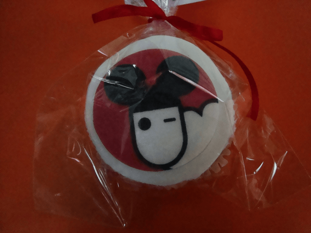 Un cupcake ambalat, cu un design care include un chip de persoană și urechile unor animale, pe un fundal roșu.