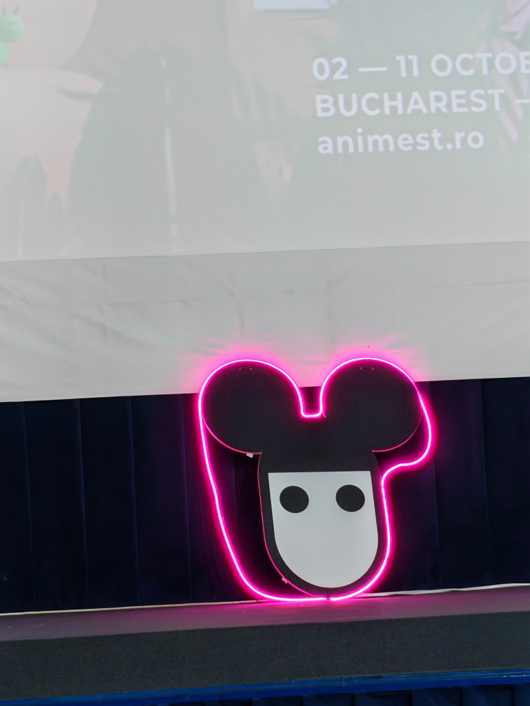 Logo neon cu o față stilizată, reprezentând un cap de animal cu urechi mari, pe un fundal cu drapaje bej și bleumarin, afișând datele unui festival de anime.